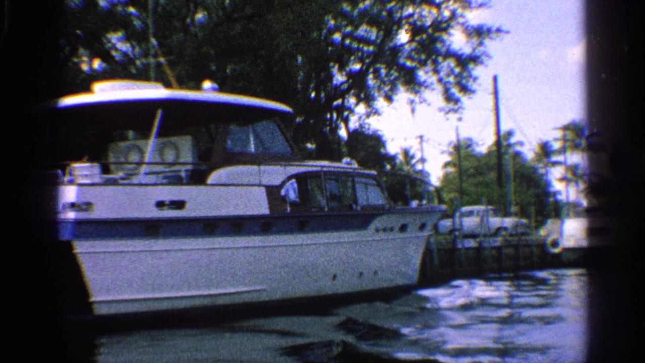 1959 California 8mm frame showing a white cabin cruiser with blue stripe moored in a palm-lined canal.