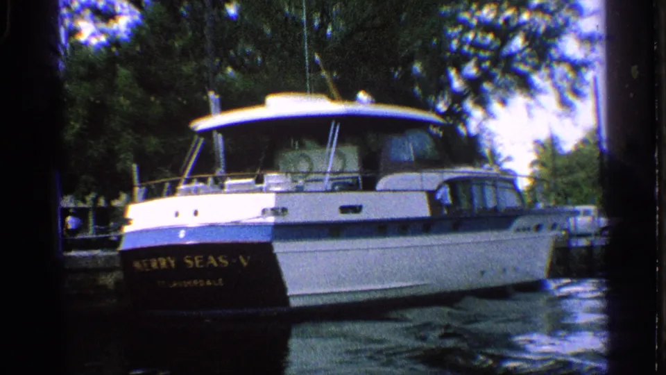 White motor yacht named MERRY SEAS-V moored in a California canal, with foliage and dock structures behind it.