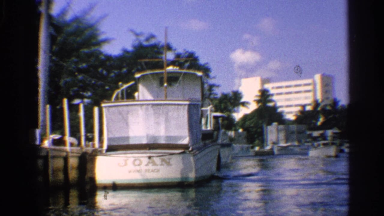 White boat named JOAN docked beside pilings on a sunny canal.