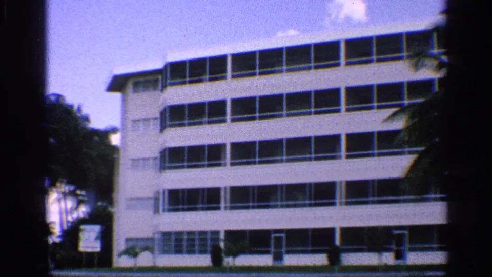 1959 California home-movie view of a modern multi-story building near palms and waterfront landscaping.