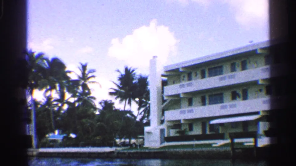 White waterfront hotel with balconies, palm trees, and lawn in a 1959 California travel scene.