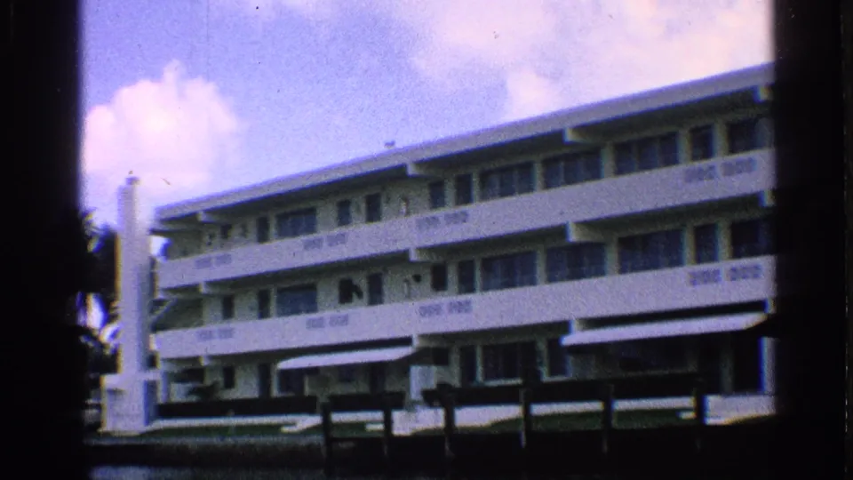 1959 California 8mm frame showing a white hotel facade with balconies, awnings, and waterfront railing.