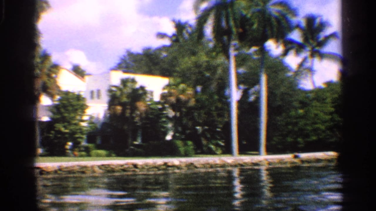 1959 California 8mm frame showing a white house behind palms and foliage along a sunny canal.