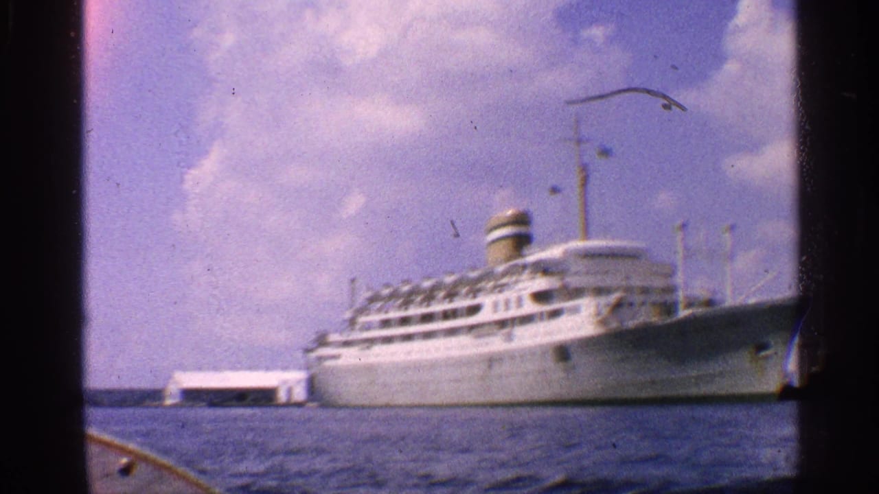 1959 California 8mm frame showing a large white ocean liner at dock, viewed from across blue harbor water.