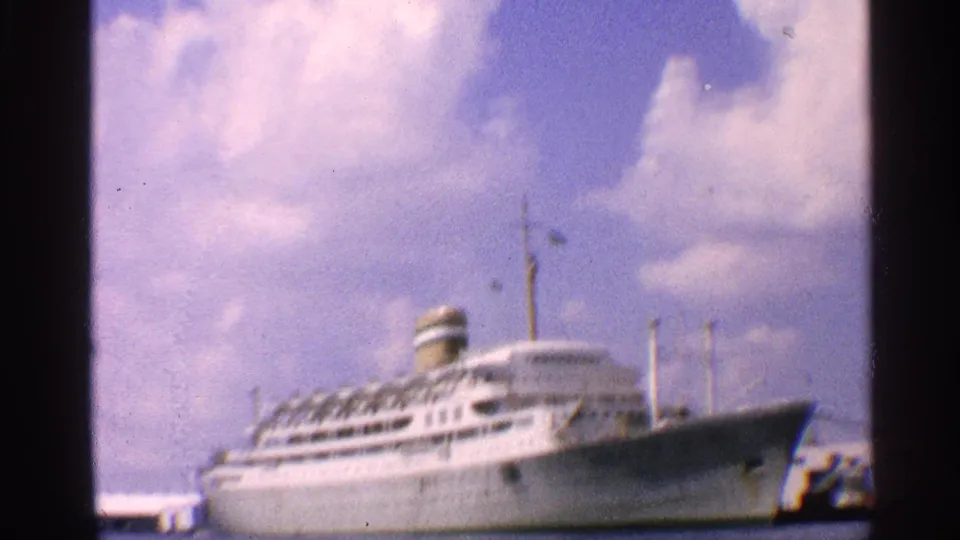 A large white liner remains docked at a California port, framed softly through 8mm film grain.