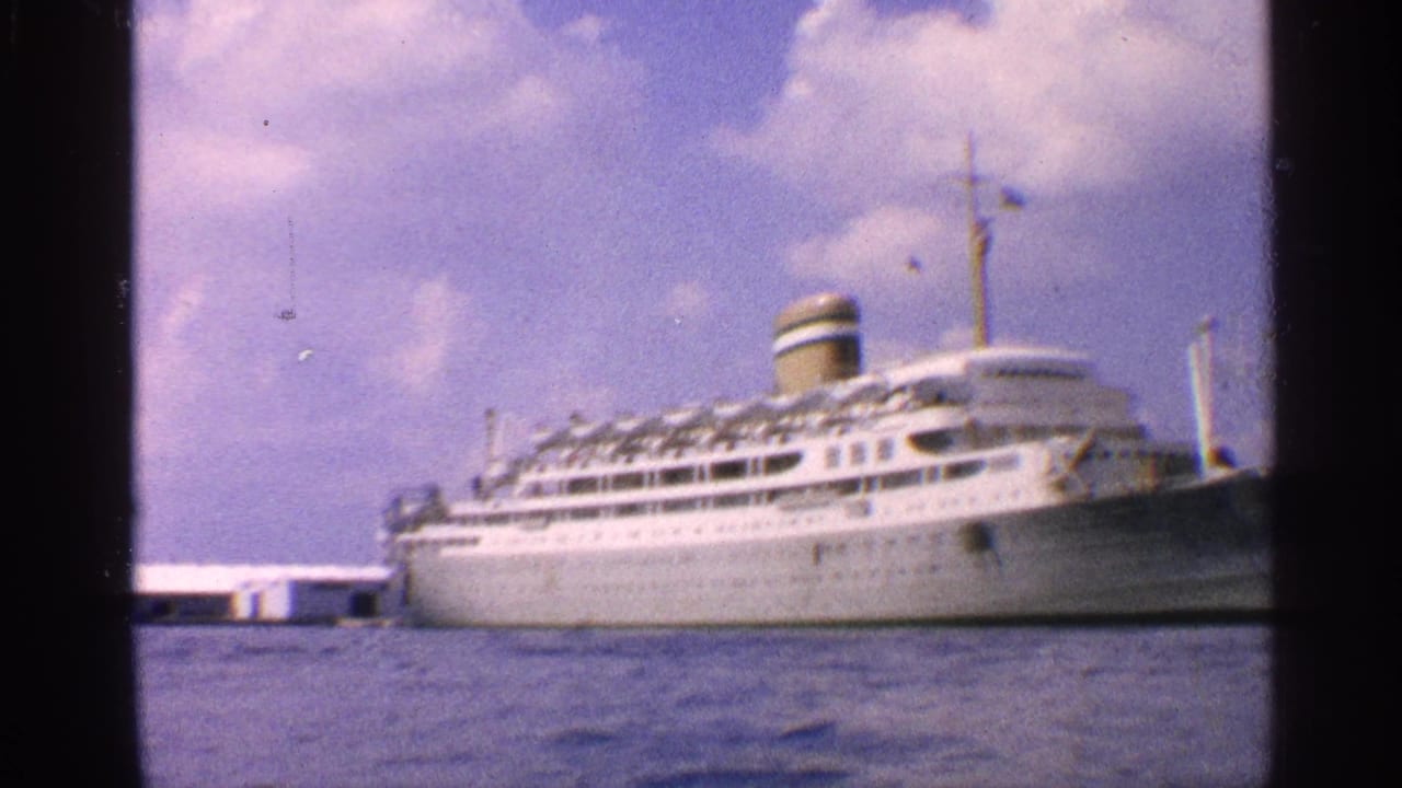 1959 California 8mm frame showing a large white multi-deck passenger ship docked at a harbor under scattered clouds.