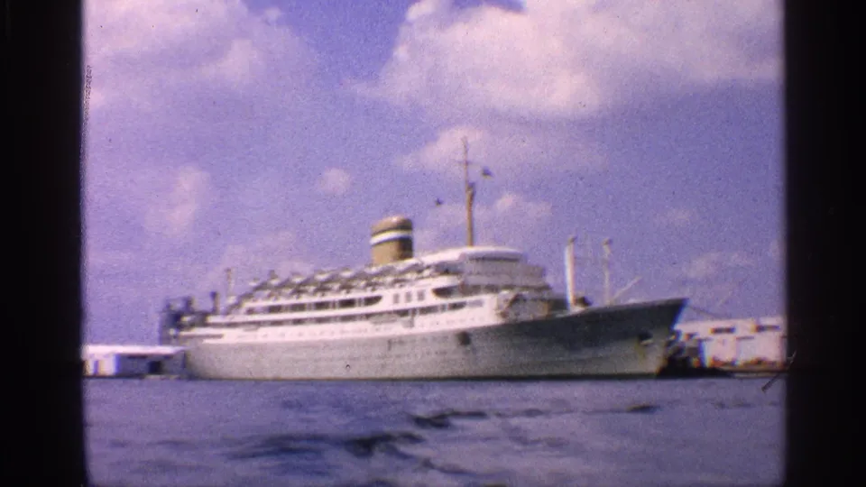 1959 California harbor view with a white ocean liner moored at a waterfront pier, seen across rippling water.