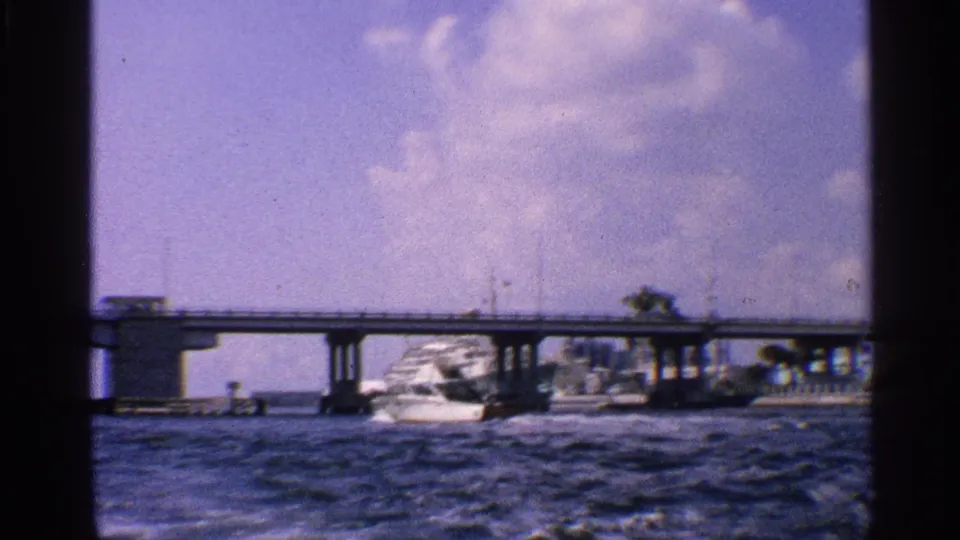 A low bridge spans choppy water while a large white vessel is visible beyond it in the California boating sequence.