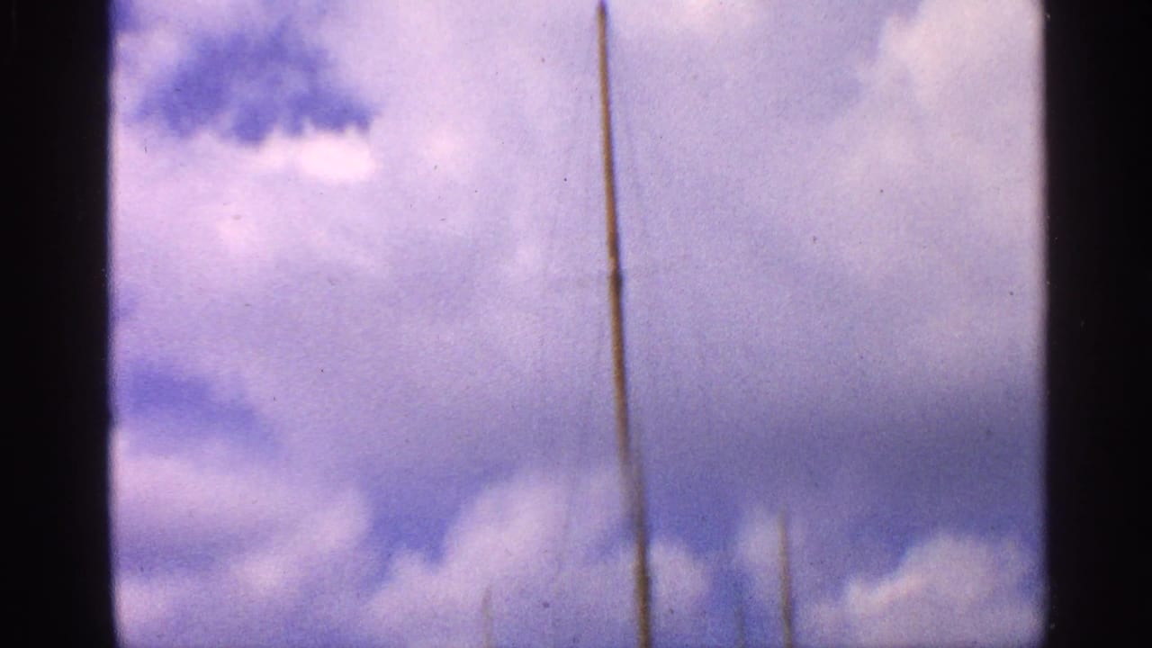 A tall mast stands against a bright cloudy sky in 1959 California 8mm marina footage.