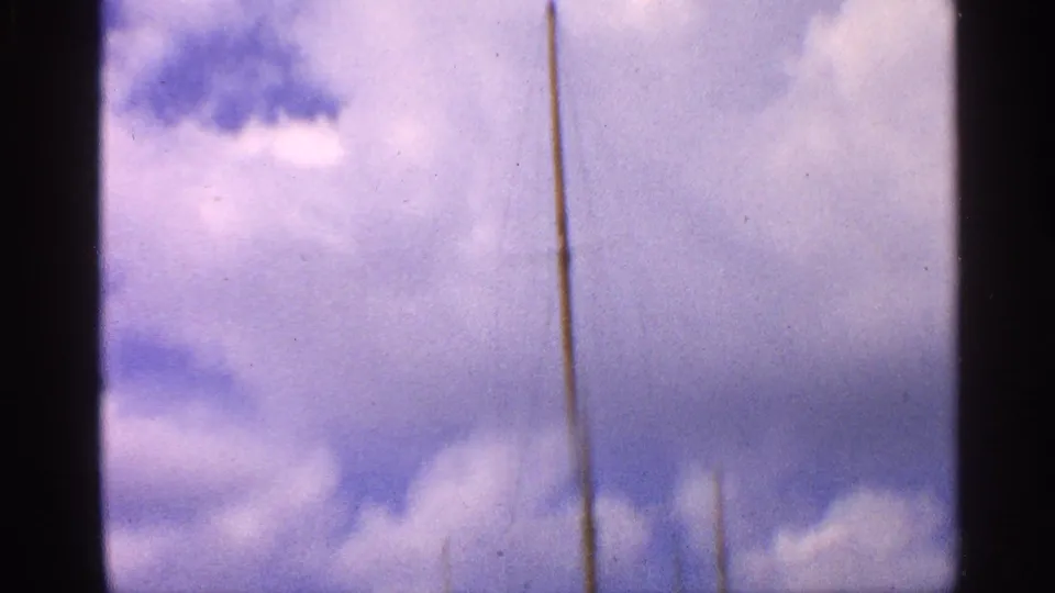 A tall mast stands against a bright cloudy sky in 1959 California 8mm marina footage.