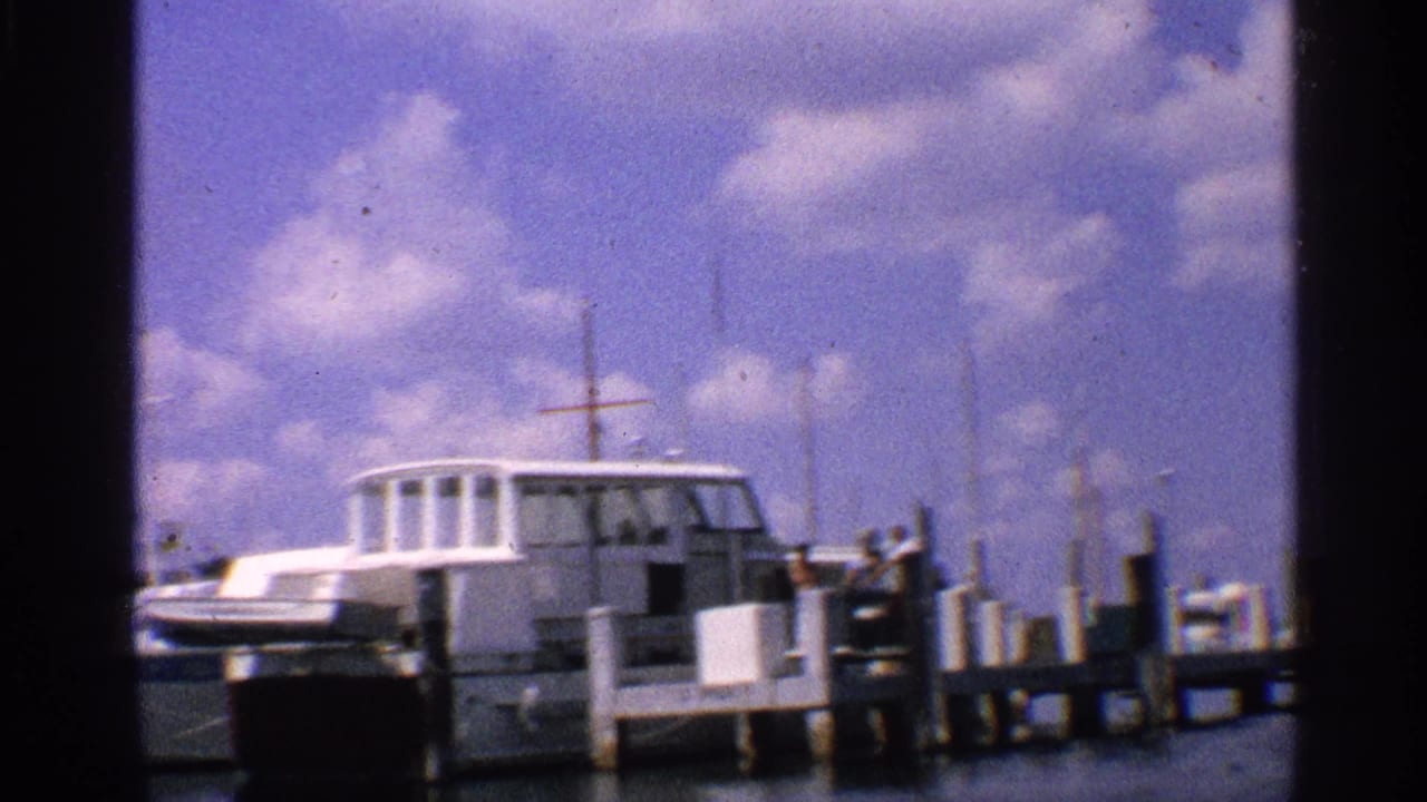 White cabin boat docked beside a wooden pier under a cloudy blue sky.