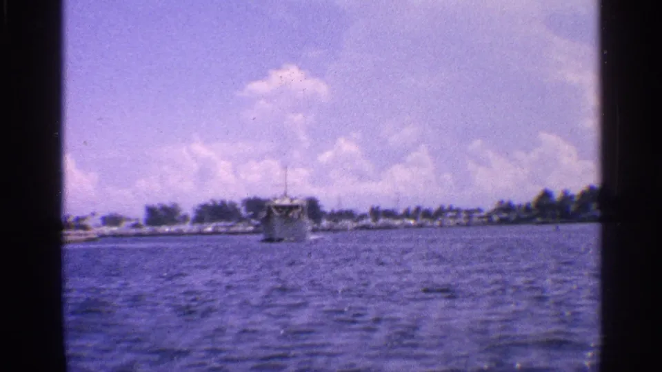 1959 California 8mm view across open water toward a small boat, low shoreline, and bright clouds.