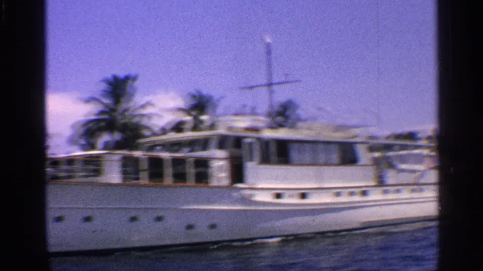 1959 Florida home-movie frame showing a white motor yacht on blue water with palm trees along the shoreline.