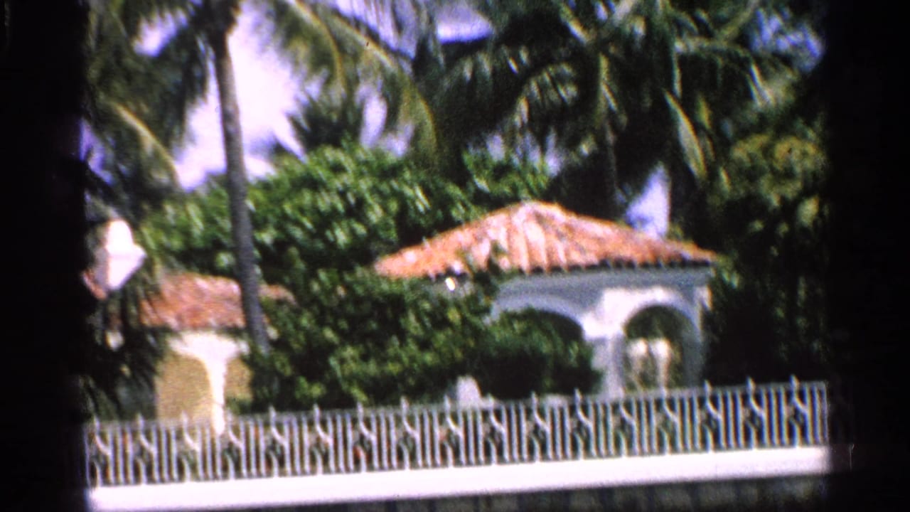 White house with terra cotta roof behind decorative fencing and palms.