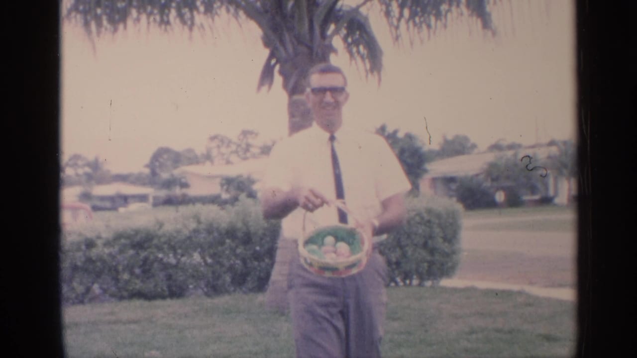 Man holding an Easter basket while standing on a lawn near a palm tree.