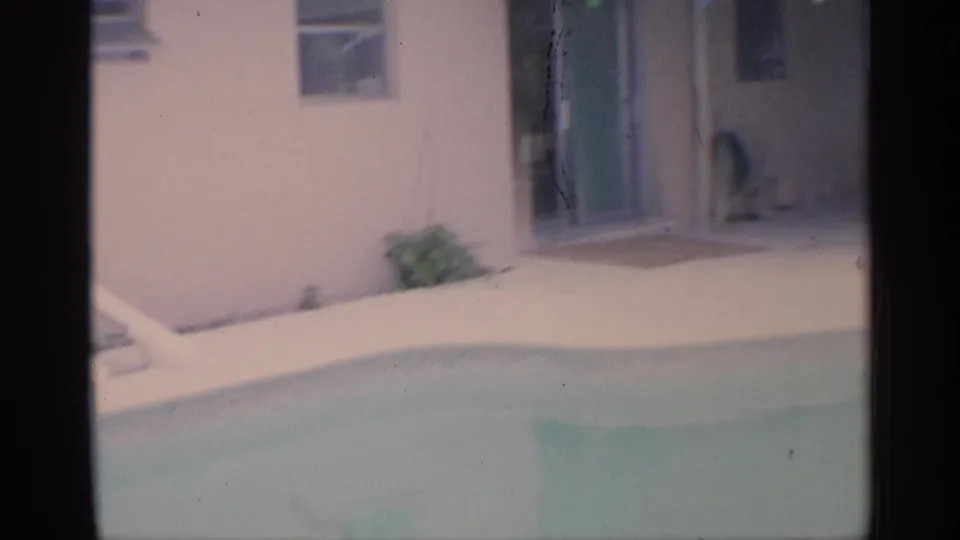 1959 Florida backyard pool view with pale house walls, sliding glass door, and patio paving visible beyond the water.