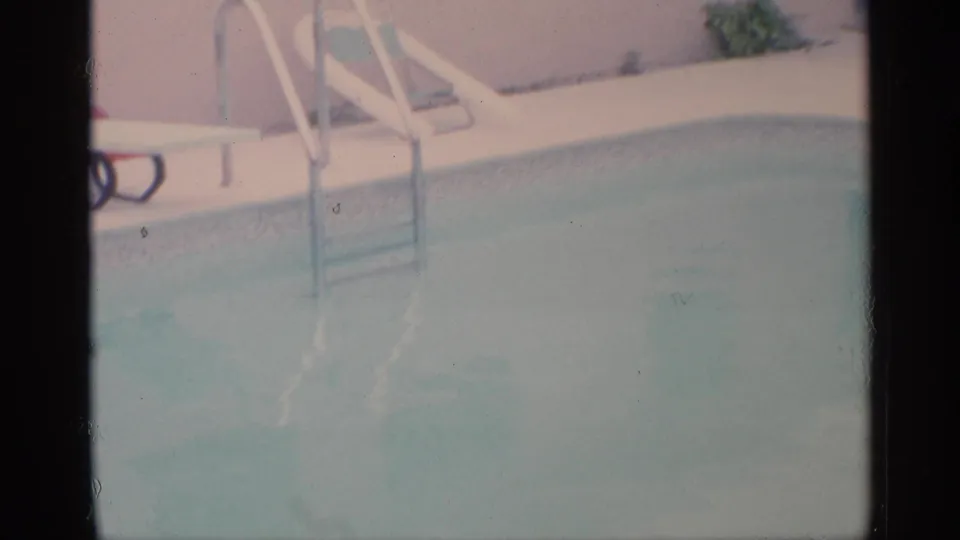 Faded 8mm frame of a Florida backyard pool, showing the metal ladder, pool edge, patio chairs, and house exterior.