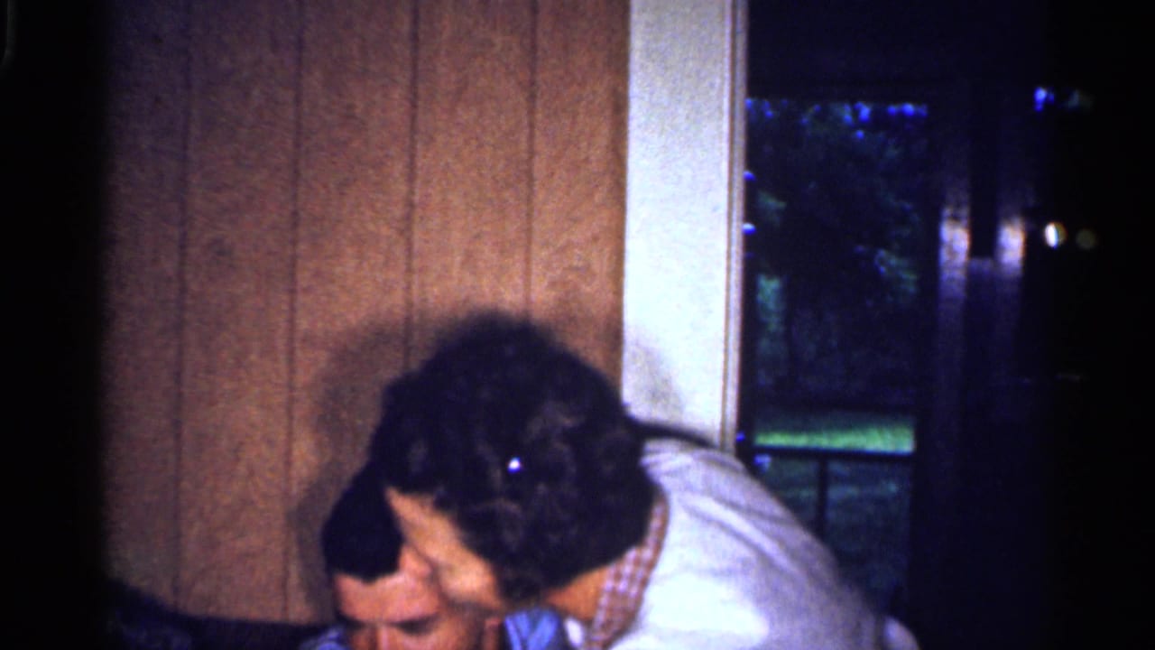 Adults leaning together in a wood-paneled room near a window.