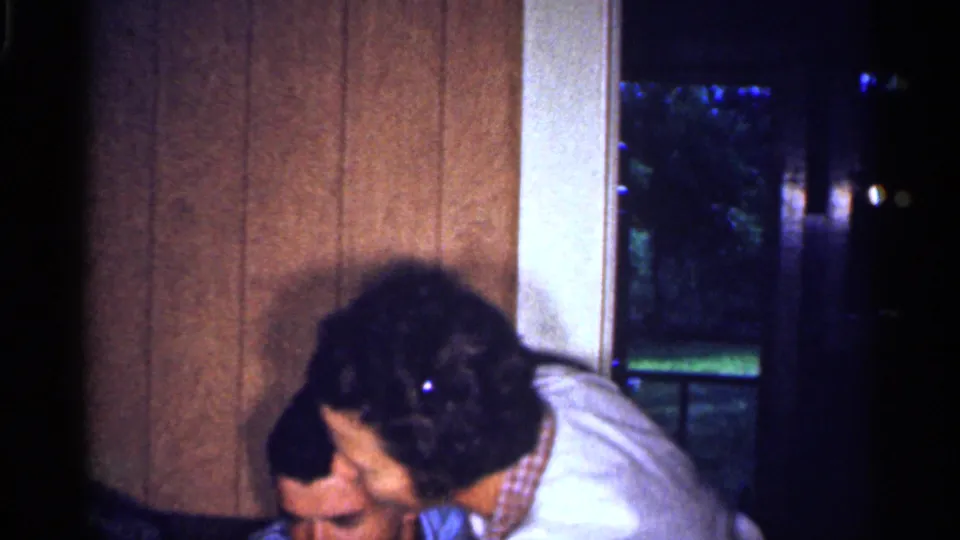 Adults appear close together inside a 1959 Florida home, with wood paneling and a dark window behind them.