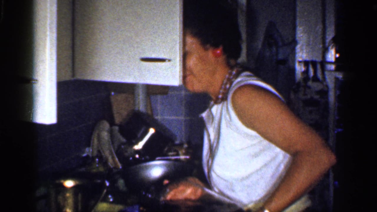 Woman in a white sleeveless top stands at a kitchen counter holding a metal pitcher.