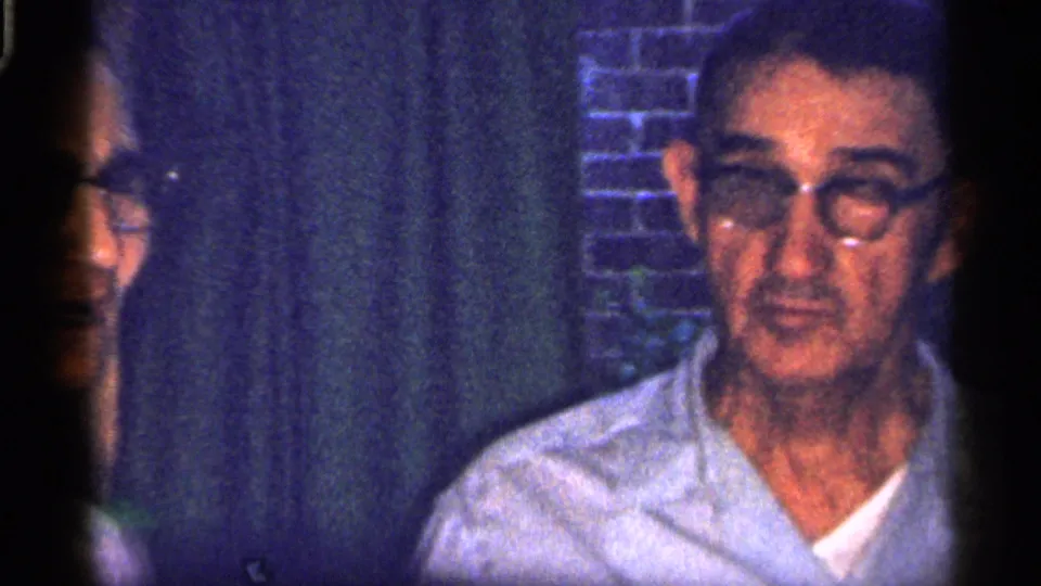 1959 Florida 8mm frame with an older man in glasses at the right edge and a partially obscured woman standing behind a dark vertical frame area.