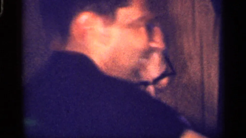 1959 Florida 8mm frame showing an older woman in glasses in side profile, softly lit against a dark interior surface.