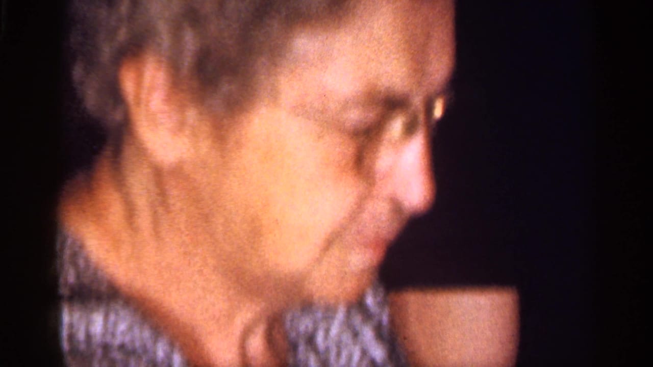 Older woman in glasses seen in soft side profile against a dark interior.