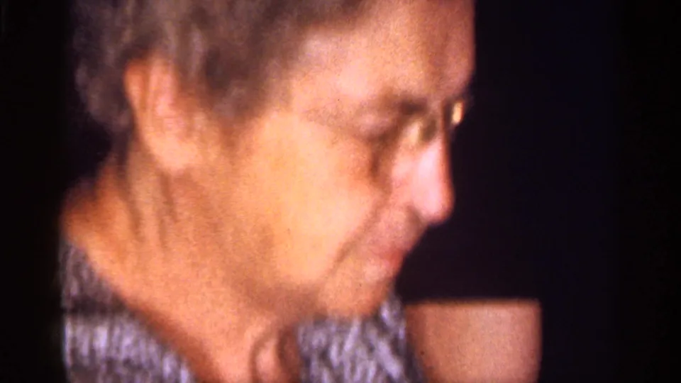 Older woman with curly gray hair and glasses in a patterned blouse, filmed indoors in 1959 Florida home-movie footage.