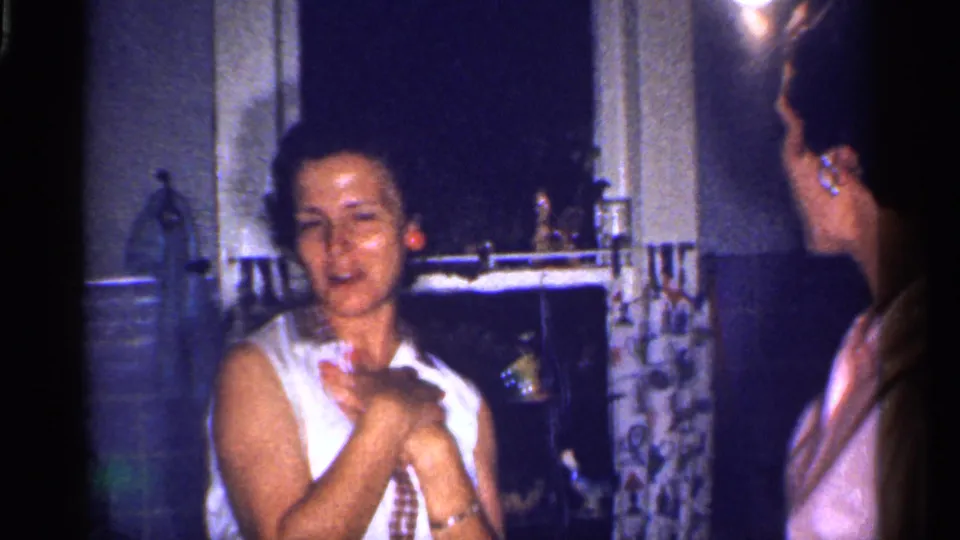 The woman in white gestures near her chest while looking toward another woman in a pink shirt inside the Florida kitchen.