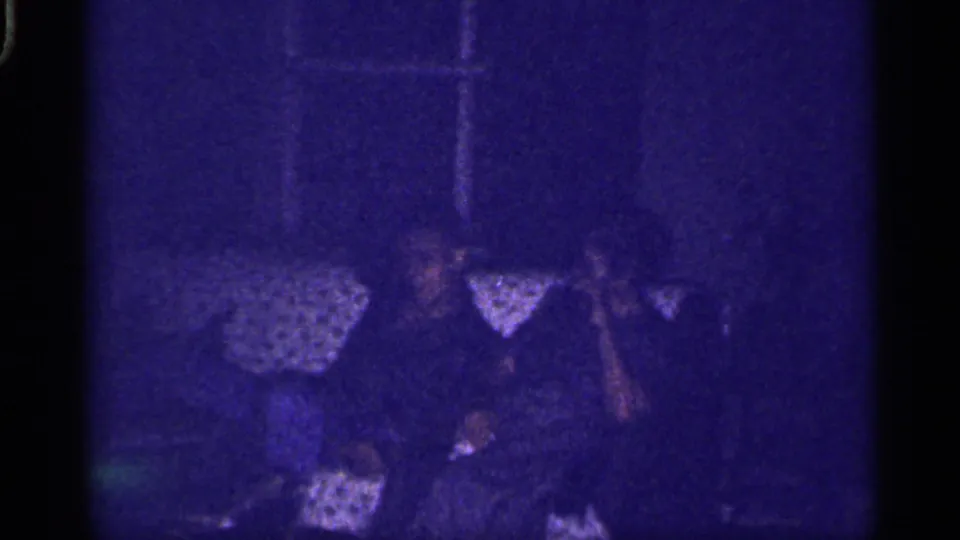 1959 Florida home-movie frame showing family members seated close together on a patterned couch in a dim interior.