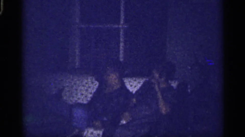 1959 Florida home-movie frame of family members on a patterned couch, partly obscured by darkness and film color shift.
