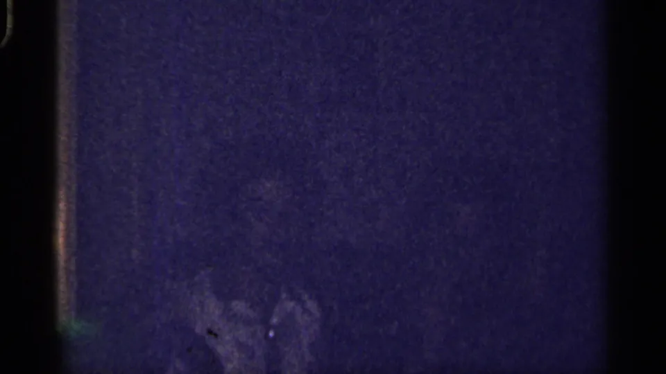 Low-light 1959 Florida home-movie frame with a faint adult figure partly visible near the bottom of a shadowed interior.