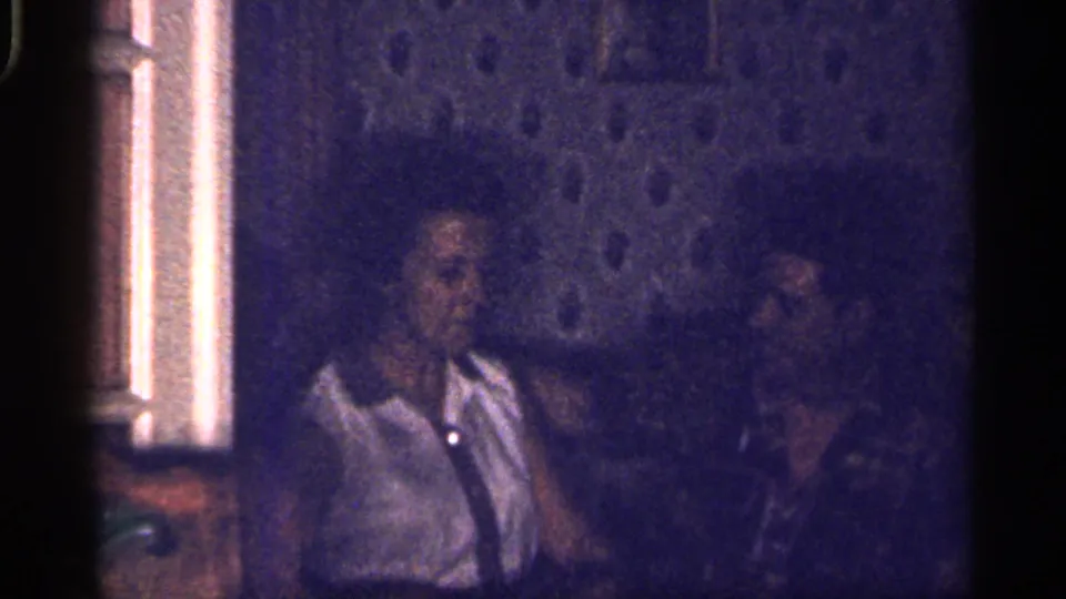 1959 Florida 8mm frame showing two adults seated indoors, the woman in a white collared shirt and the man partly visible beside her.