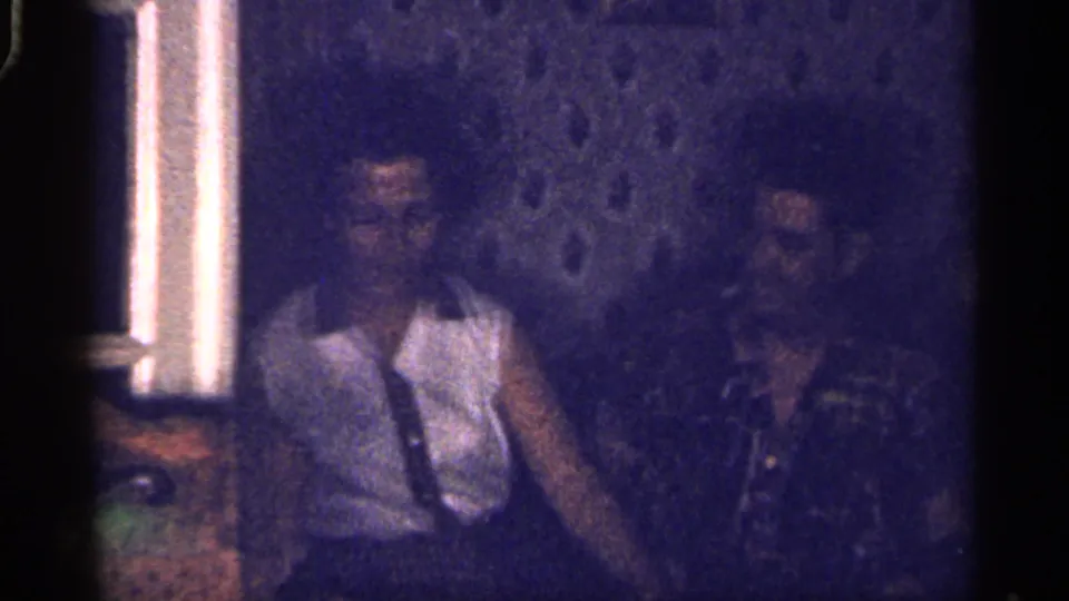 1959 Florida 8mm frame of two adults seated close together, with soft focus and a purple cast over the room.