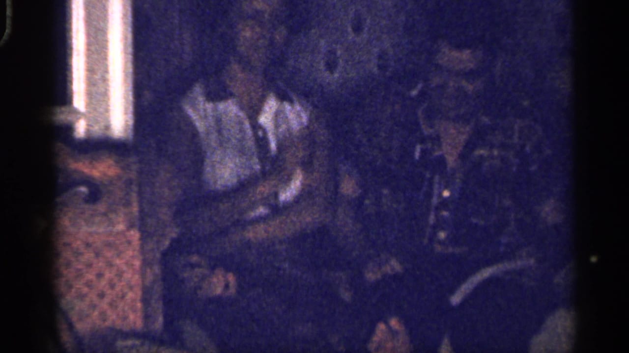 Dim living room with adults seated near a curtained window, partly obscured by 8mm shadow.