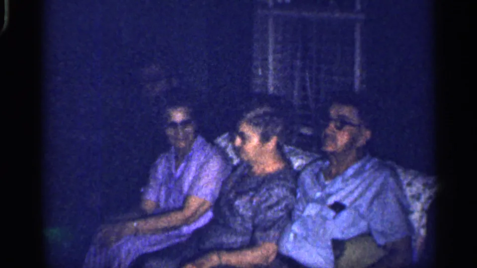In this 1959 Florida home-movie still, four people sit together in a living room, their faces softened by grain and low exposure.