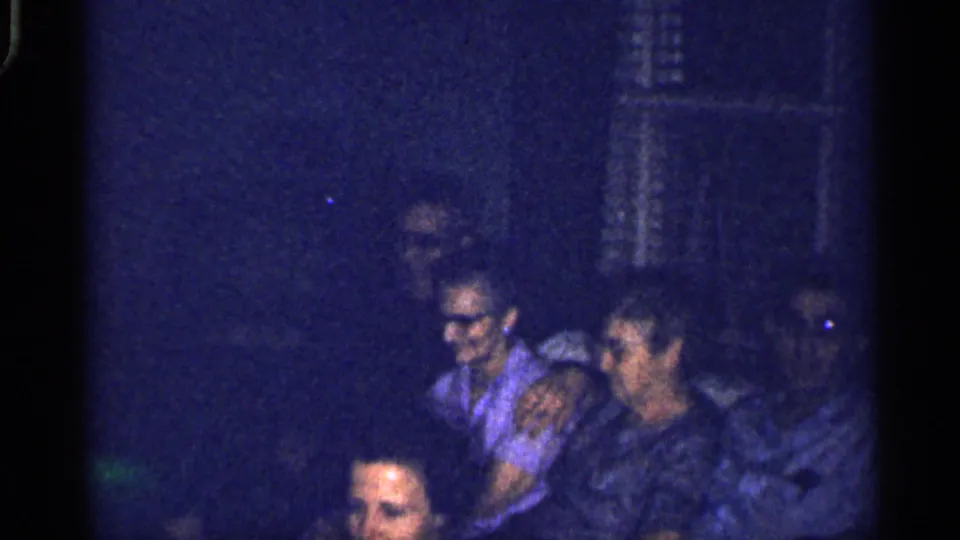 Blue-tinted 8mm frame from a 1959 Florida family gathering, showing adults seated closely on a couch.