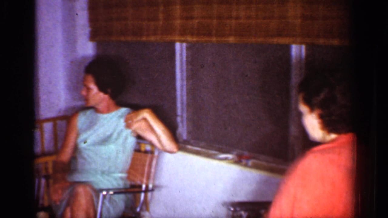 1959 Florida home-movie frame with a seated woman in a light blue dress and another person partly visible indoors.