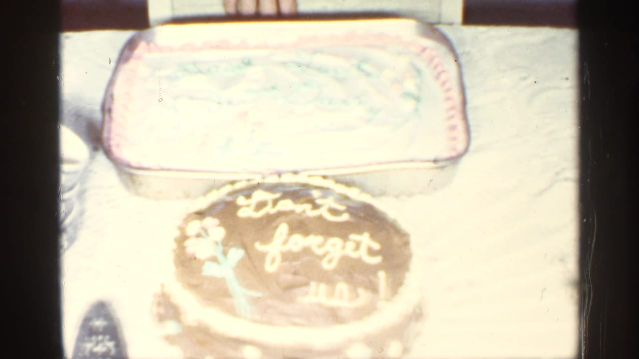 A table holds a chocolate cake with white icing reading "Don't forget us!" and a rectangular frosted cake behind it.