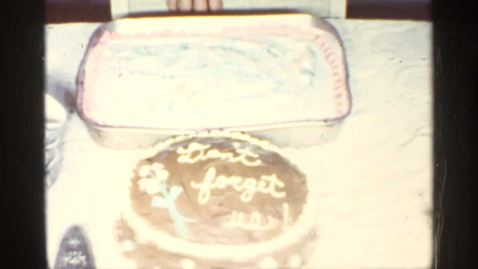 A table holds a chocolate cake with white icing reading "Don't forget us!" and a rectangular frosted cake behind it.