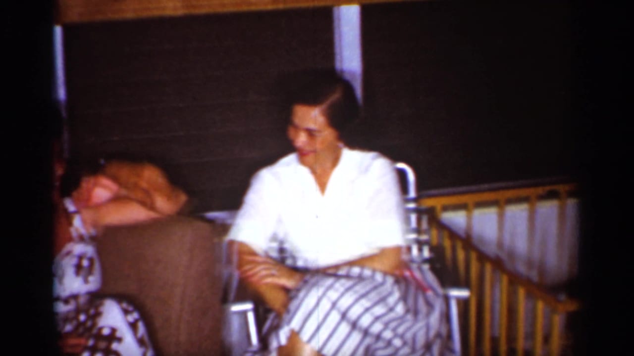 Woman in a white blouse and striped skirt sits in a living room chair near a couch.