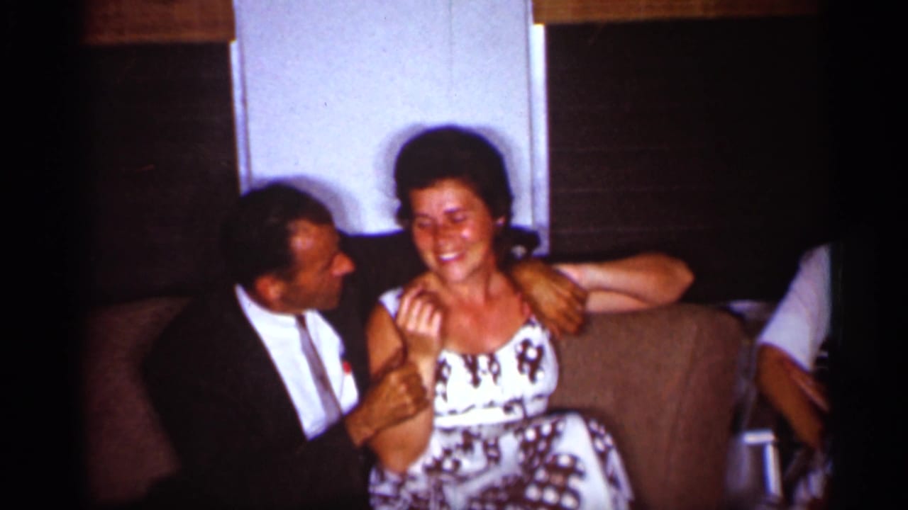 Man in a dark suit sits close to a smiling woman in a patterned dress on a couch.