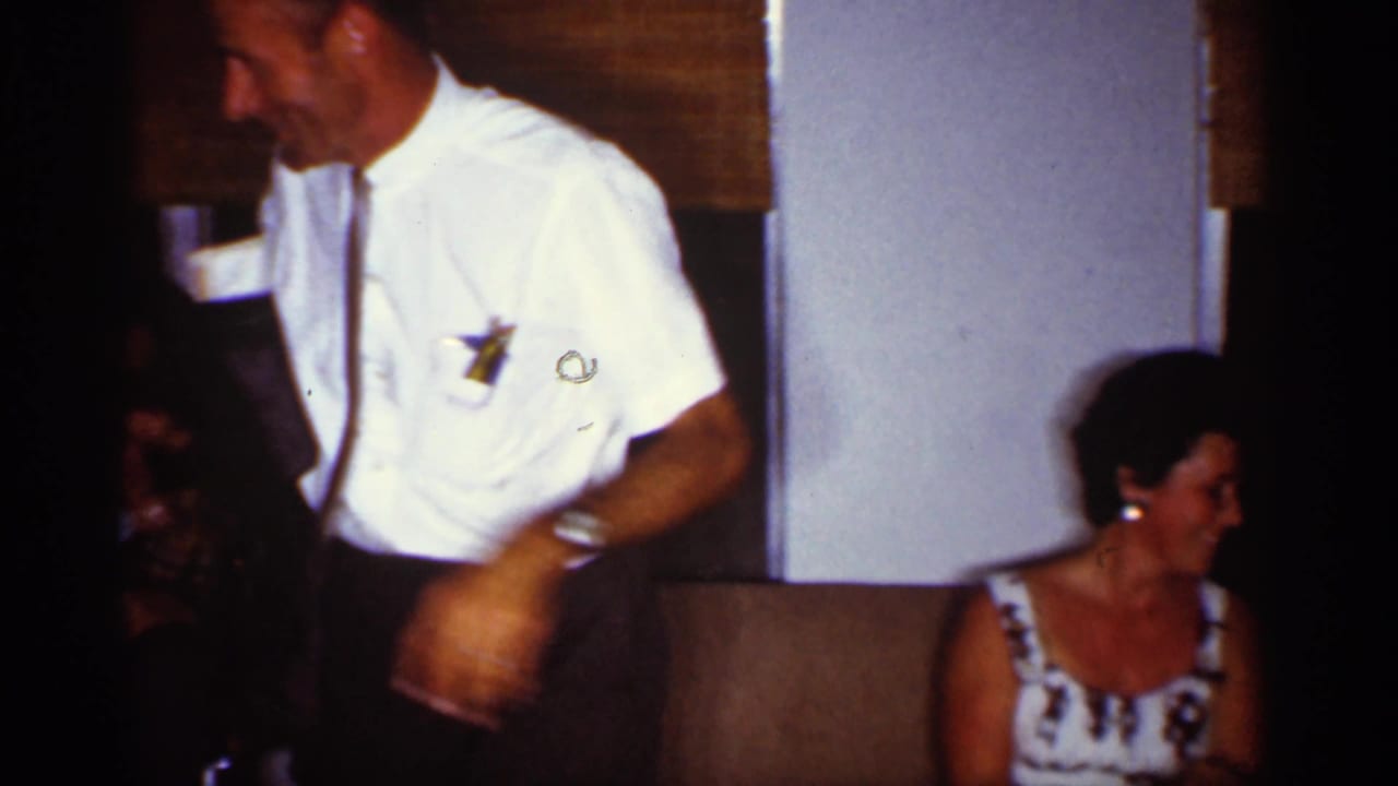 Man in a white shirt stands beside a seated woman in a patterned dress.