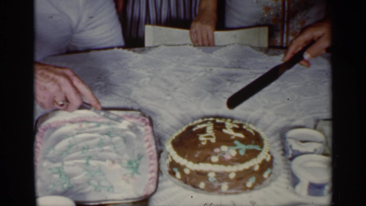 A hand and cake knife hover near two decorated cakes on a table.