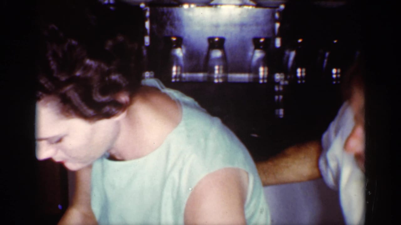 Woman in a pale green dress leans forward beside a man partly visible at right.