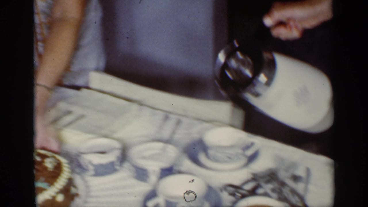 1959 Florida home-movie frame showing coffee poured from a white thermos near blue and white patterned cups on a crowded table.