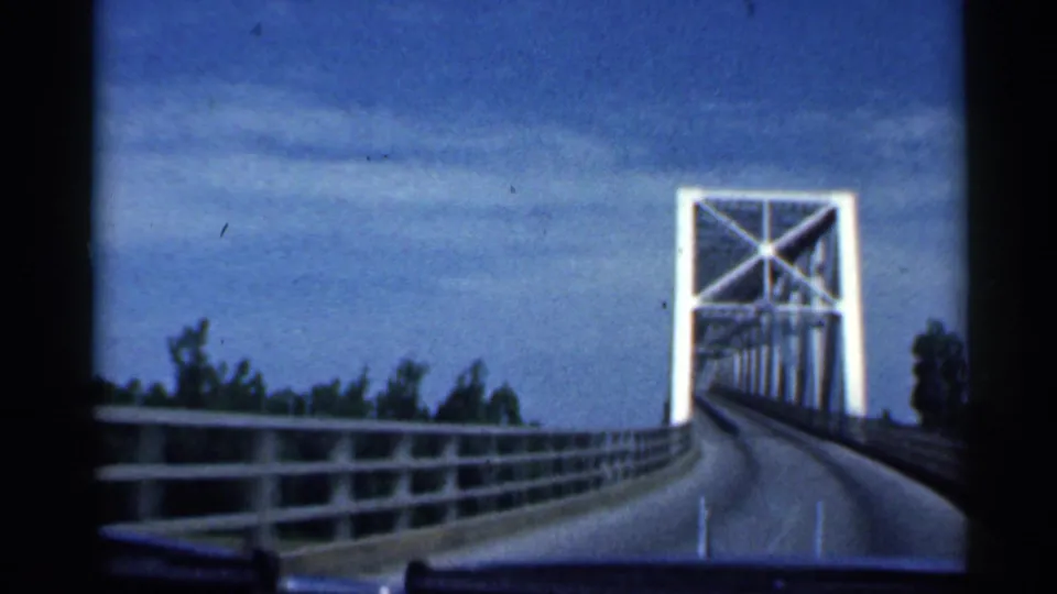 1959 Indiana home-movie view looking straight toward the white steel truss bridge as the road and guardrails lead into the structure.
