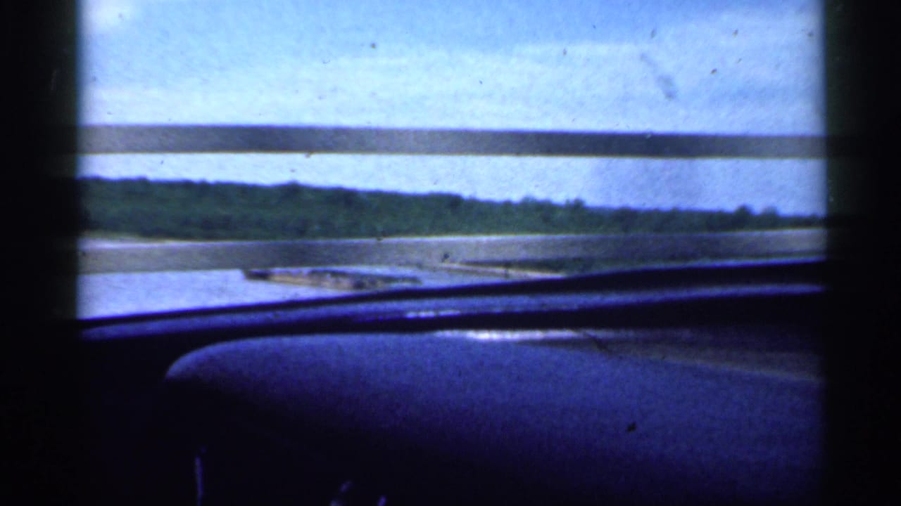 View from inside a car crossing a river bridge with guardrail and shoreline beyond.