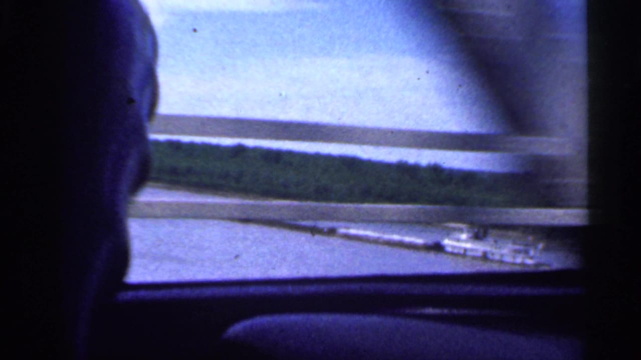 Driver's head silhouette appears in a 1959 Indiana car-window view over a river bridge and wooded bank.