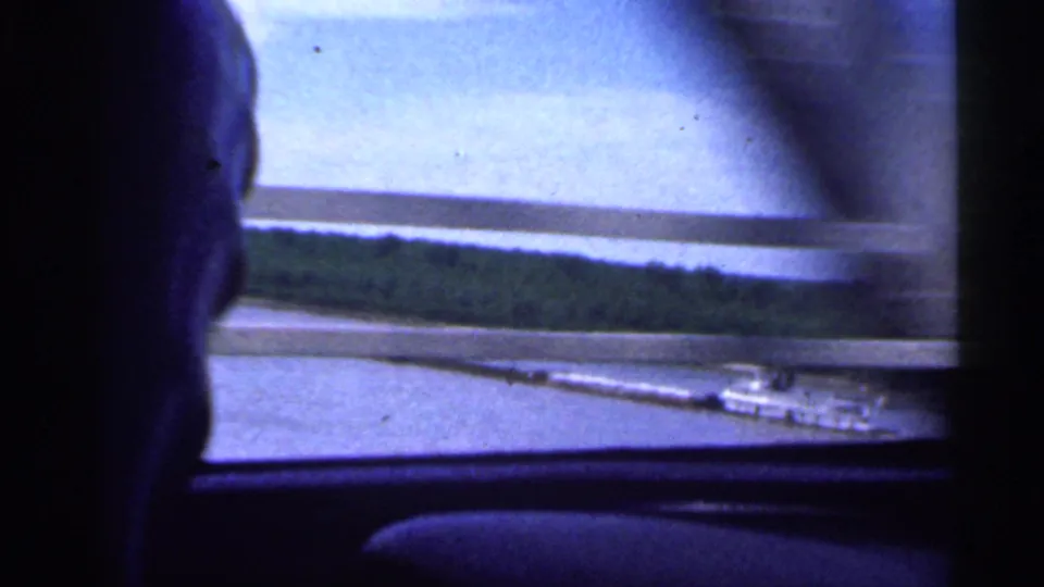 Driver's head silhouette appears in a 1959 Indiana car-window view over a river bridge and wooded bank.